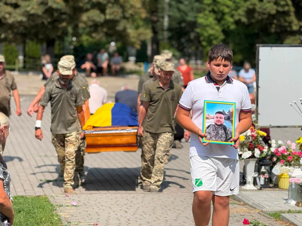 Хлопець із портретом воїна на похороні під українським прапором