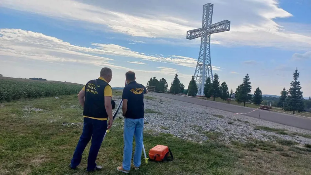 Двоє чоловіків оглядають великий металевий хрест на пагорбі