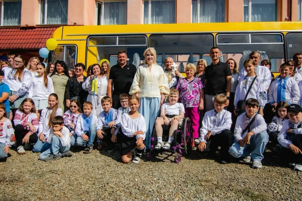 Група дітей і дорослих біля жовтого автобуса