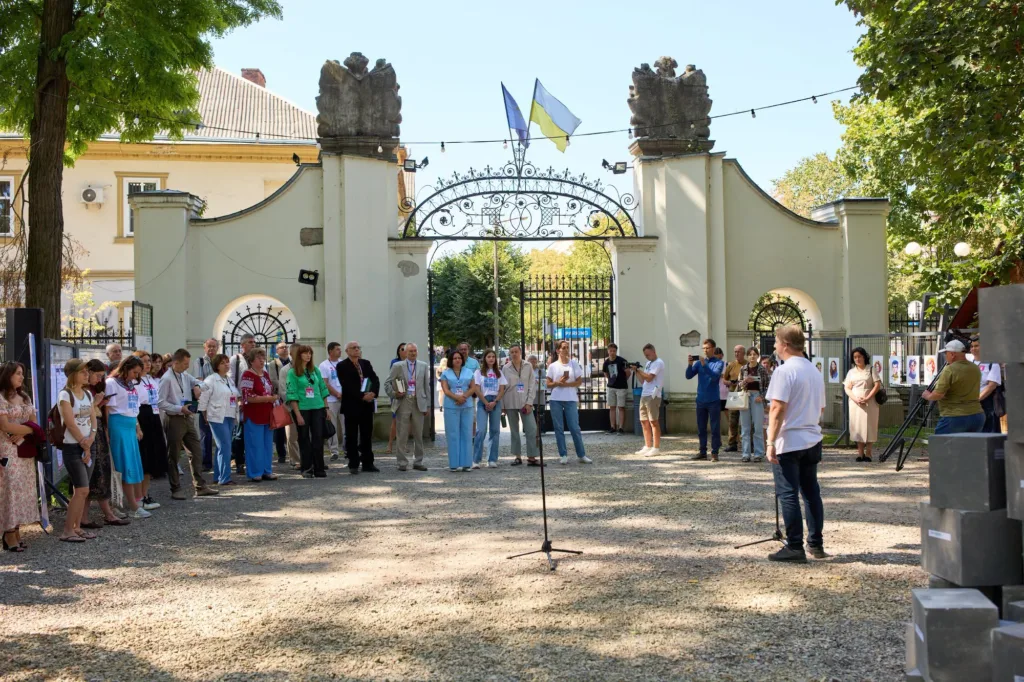 Люди слухають промову біля воріт з українським прапором