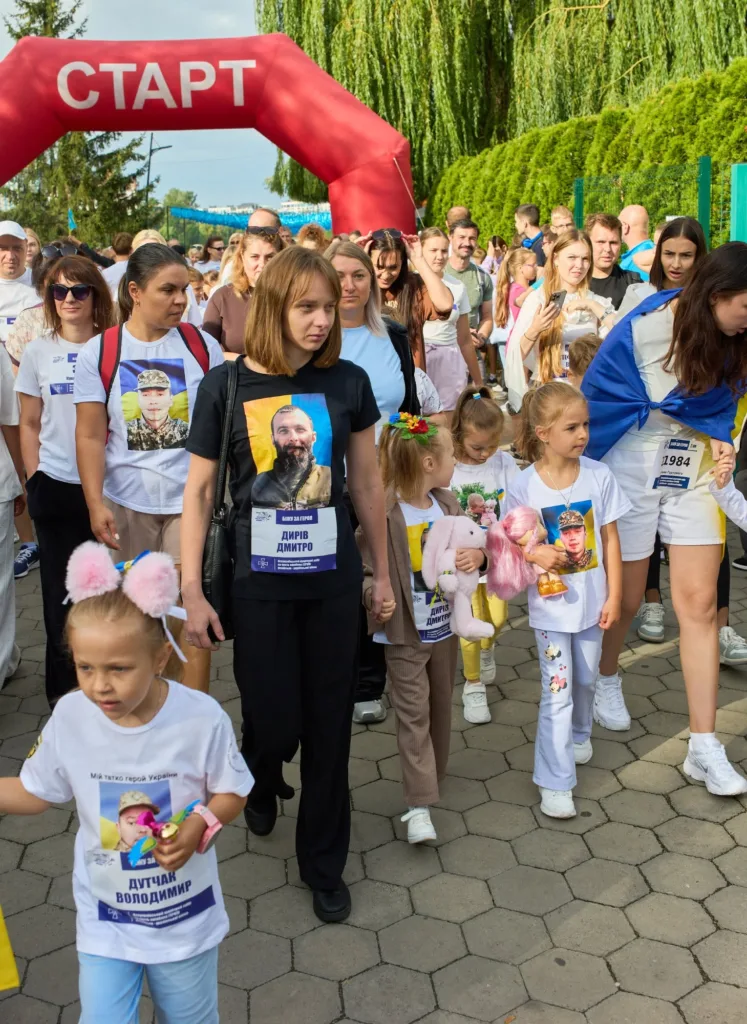 Учасники забігу під аркою «Старт» із портретами захисників