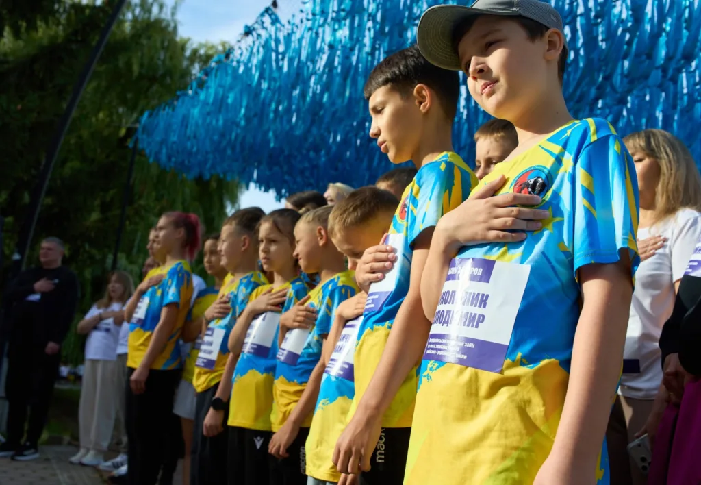 Діти у синьо-жовтих футболках стоять із руками на серці