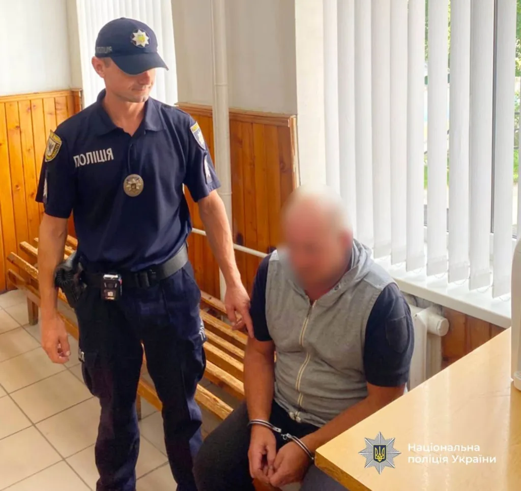 Поліцейський стоїть поруч із затриманим у кайданках