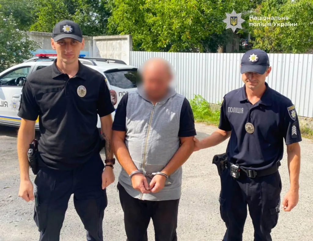 Поліцейські супроводжують чоловіка в кайданках біля патрульного авто