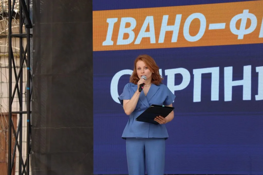 Ведуча в синьому костюмі виступає на сцені