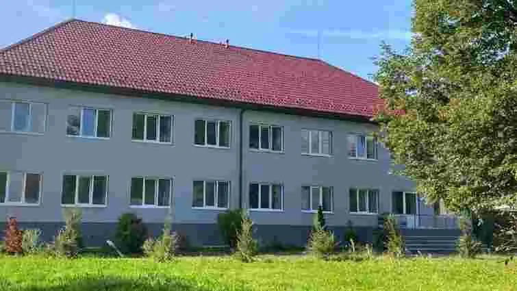 Двоповерхова будівля з червоним дахом серед зелені