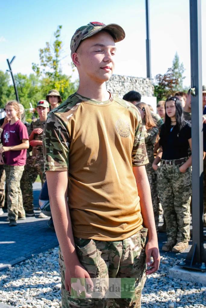 Юнак у камуфляжі стоїть перед групою людей