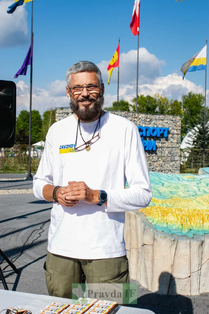Усміхнений чоловік у футболці ZAVZHDY UA біля прапорів