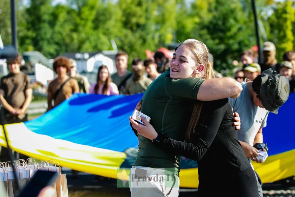 Дві жінки обіймаються біля автомобіля з українським прапором