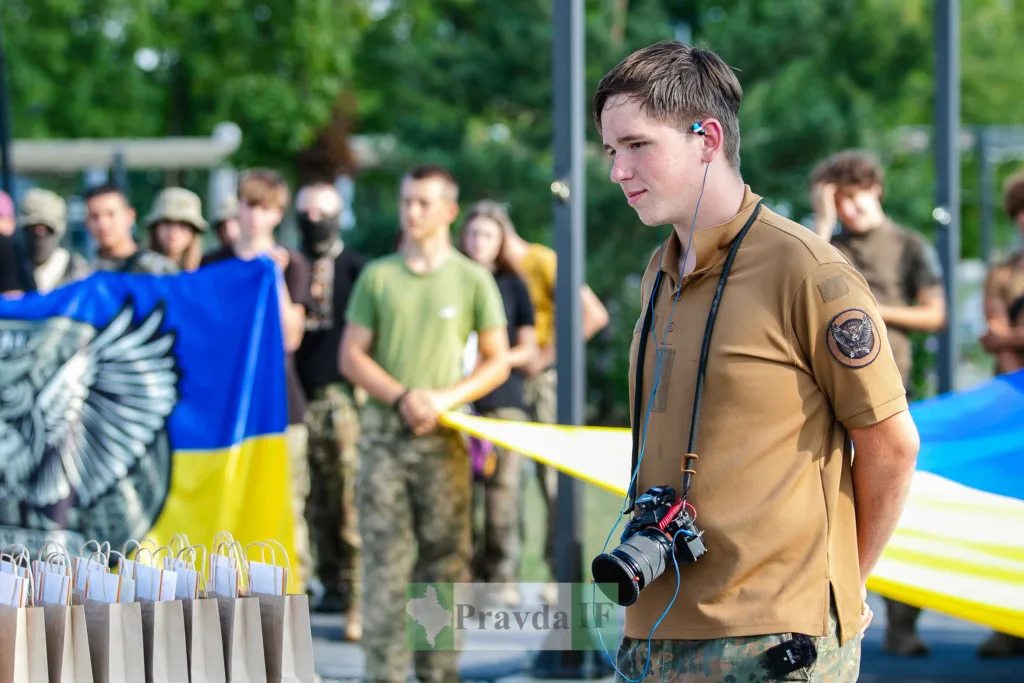 Чоловік із камерою біля українського прапора та військових