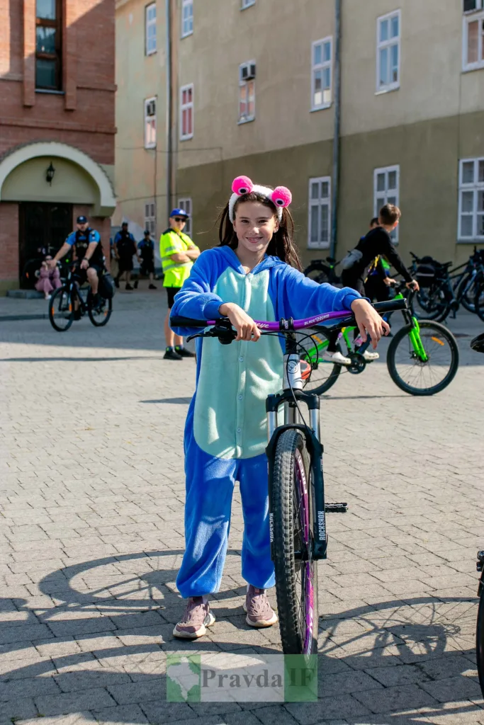Дівчинка в синьому костюмі стоїть із велосипедом