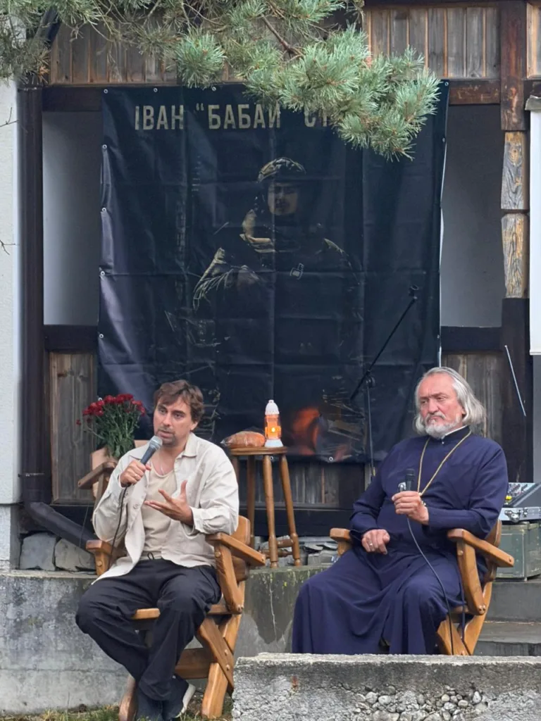 Двоє чоловіків із мікрофонами біля меморіального банера