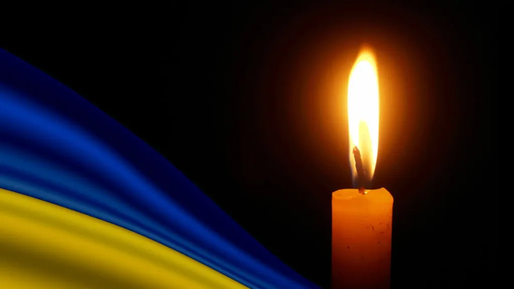 Запалена свічка поруч із синьо-жовтим прапором України