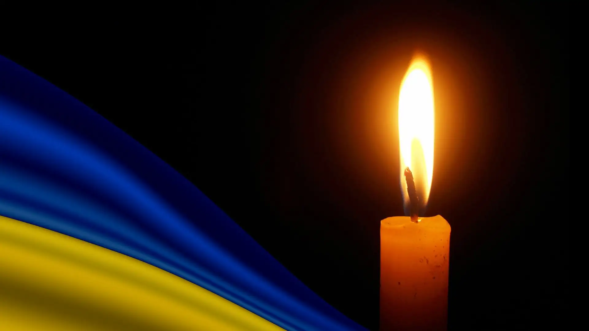 Запалена свічка поруч із синьо-жовтим прапором України