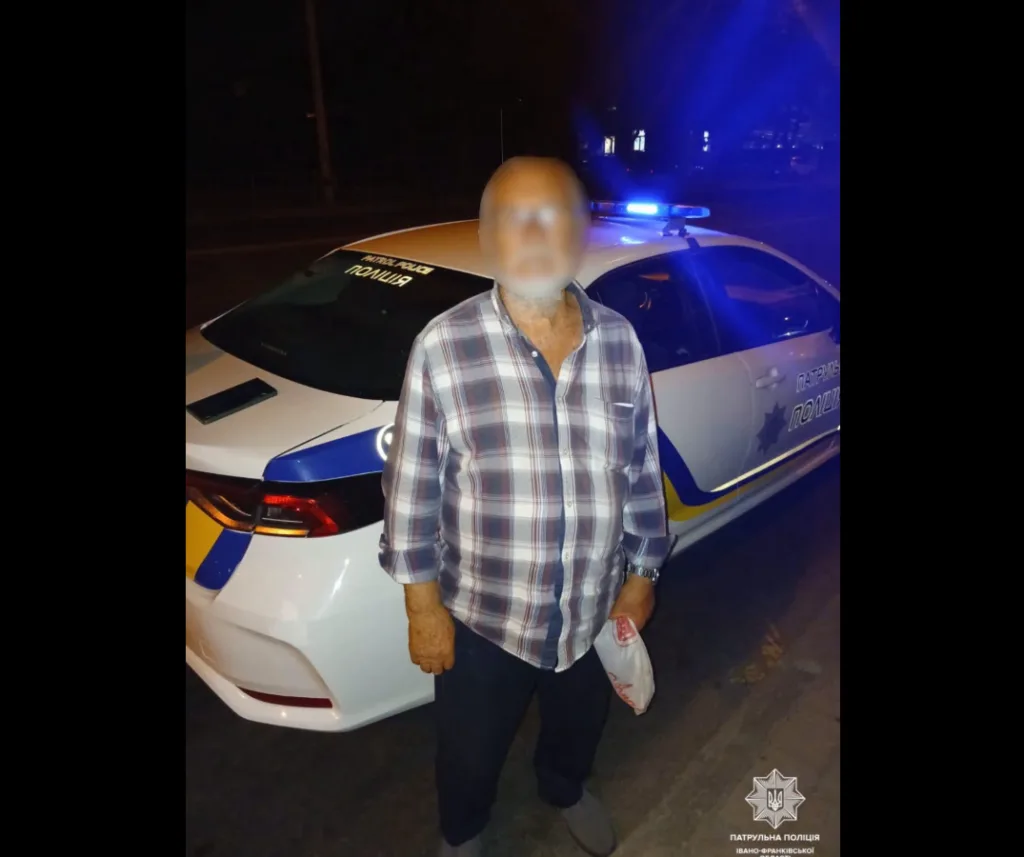 Чоловік стоїть біля патрульного автомобіля вночі
