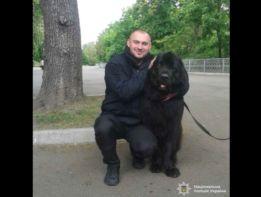 Поліцейський позує з великим чорним собакою в парку