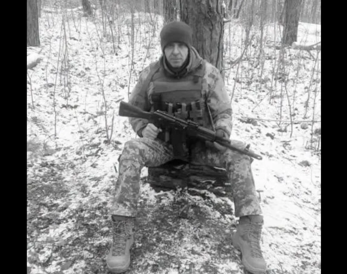 Військовий із гвинтівкою сидить у засніженому лісі