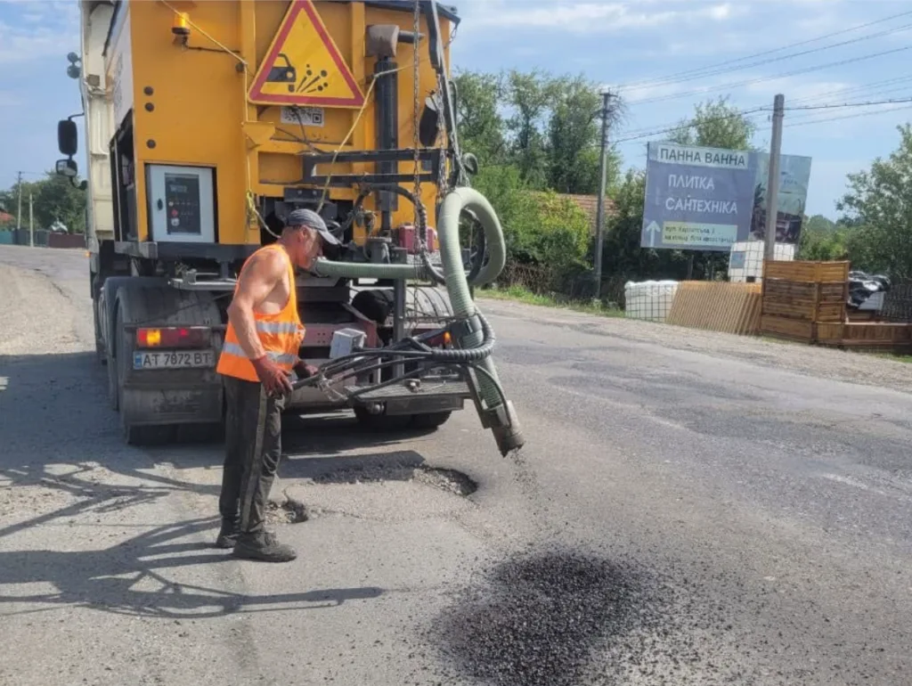 Дорожній працівник ремонтує асфальт біля спеціальної машини
