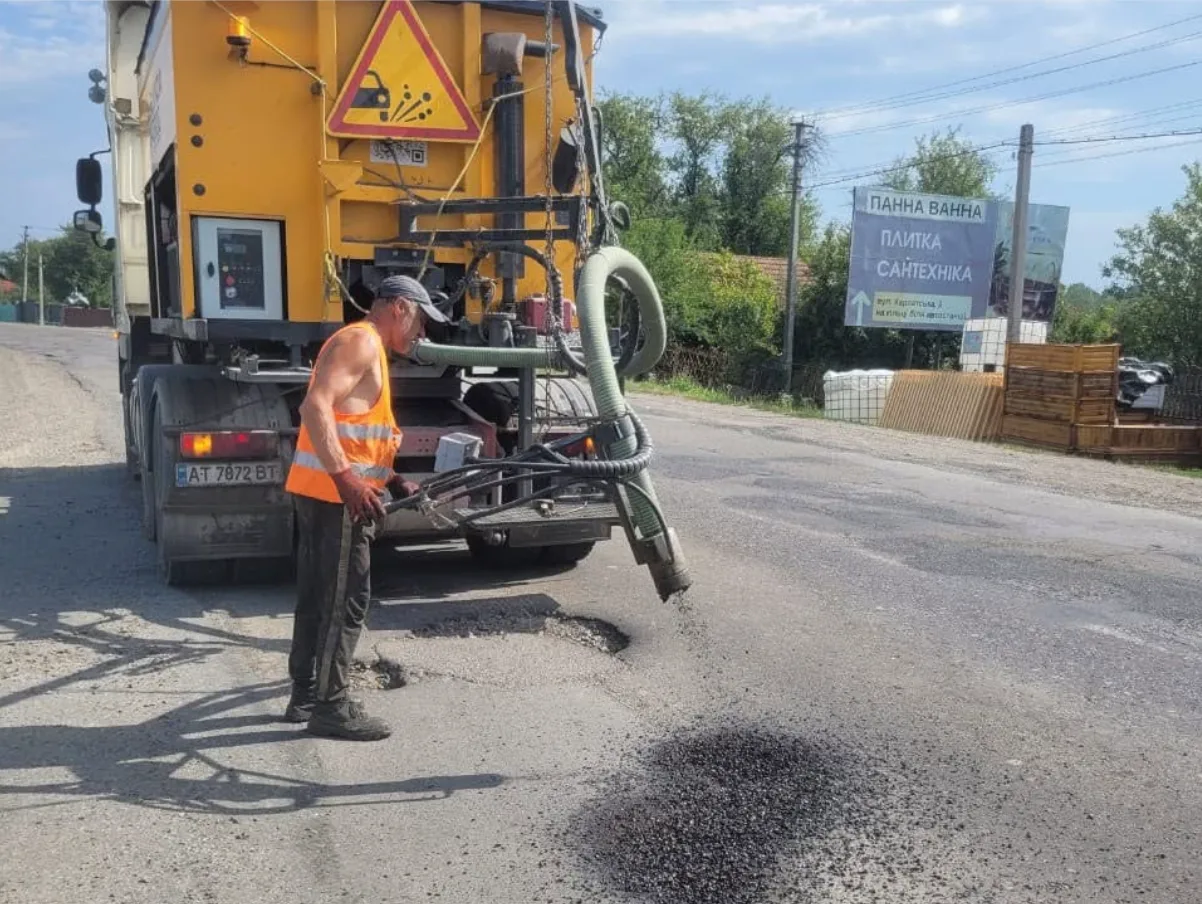 Дорожній працівник ремонтує асфальт біля спеціальної машини