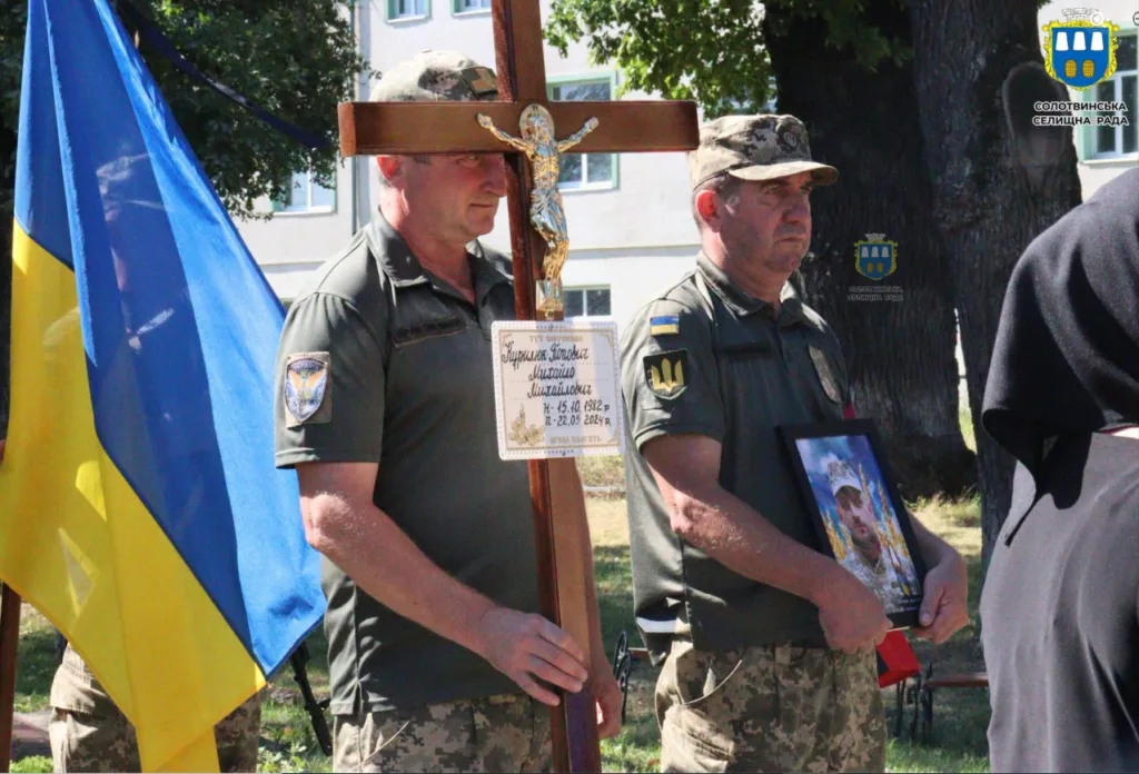 Військові тримають хрест і портрет загиблого біля прапора