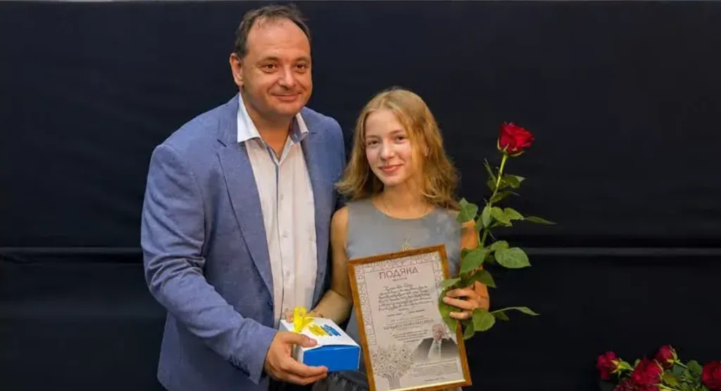 Чоловік вітає дівчину з грамотою та трояндою