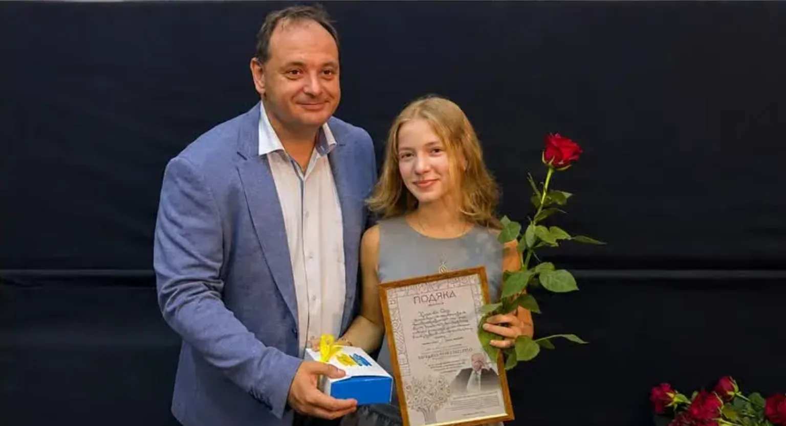 Чоловік вітає дівчину з грамотою та трояндою