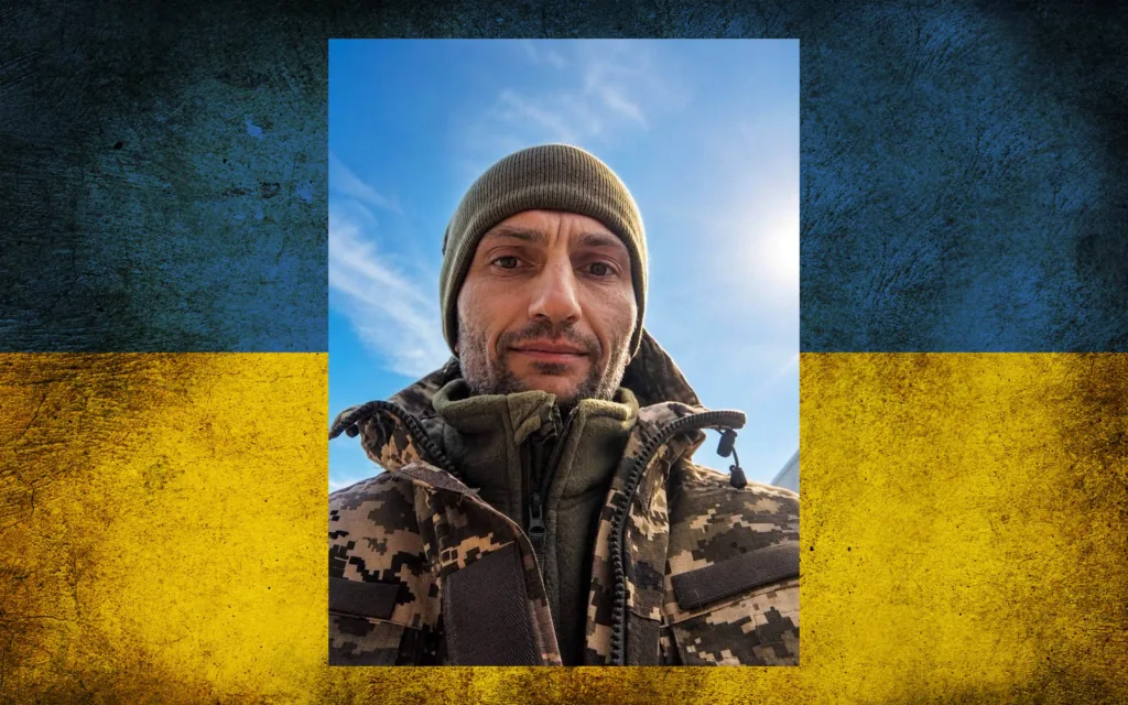 Чоловік у камуфляжі на тлі українського прапора