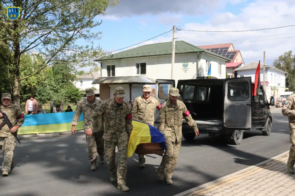 Військові несуть труну, вкриту українським прапором