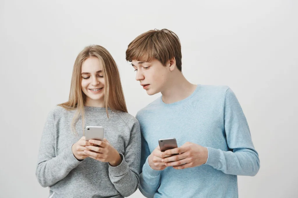 Двоє підлітків користуються смартфонами на світлому тлі