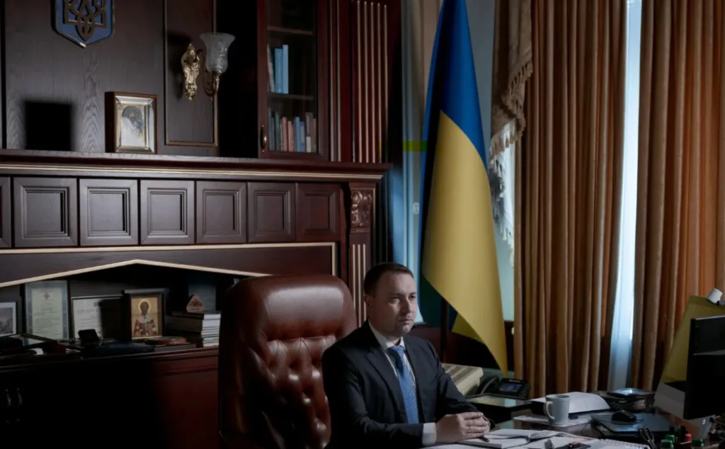 Посадовець сидить за столом поруч із прапором України