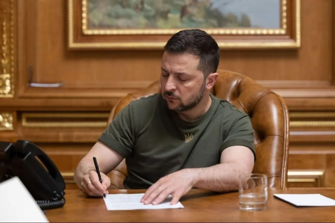Володимир Зеленський підписує документ за робочим столом