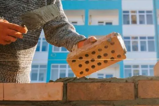 Муляр кладе цеглу на розчин біля будівлі