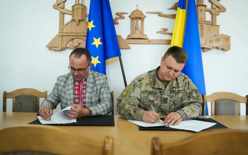 Чоловіки підписують документи біля прапорів України та ЄС