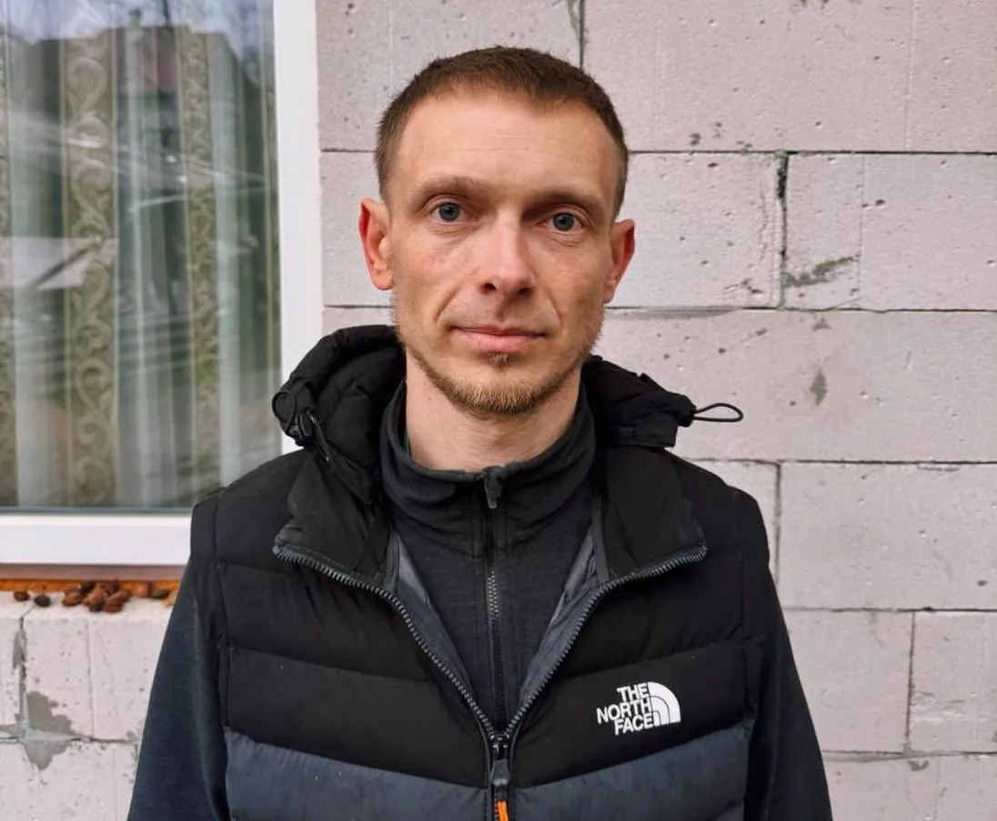 Чоловік у чорній куртці біля цегляної стіни