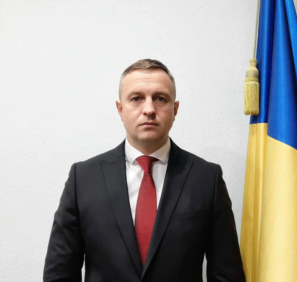 Чоловік у костюмі стоїть поруч із прапором України