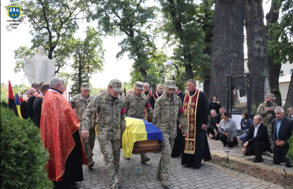 Військові несуть труну, вкриту українським прапором
