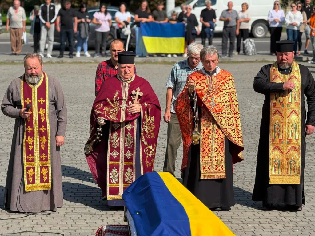 Священники моляться над труною, вкритою українським прапором
