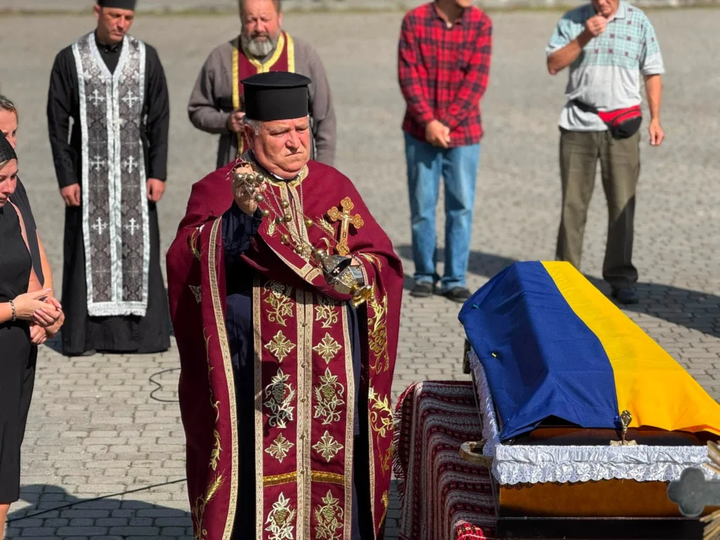 Священник кадить біля труни, вкритої українським прапором