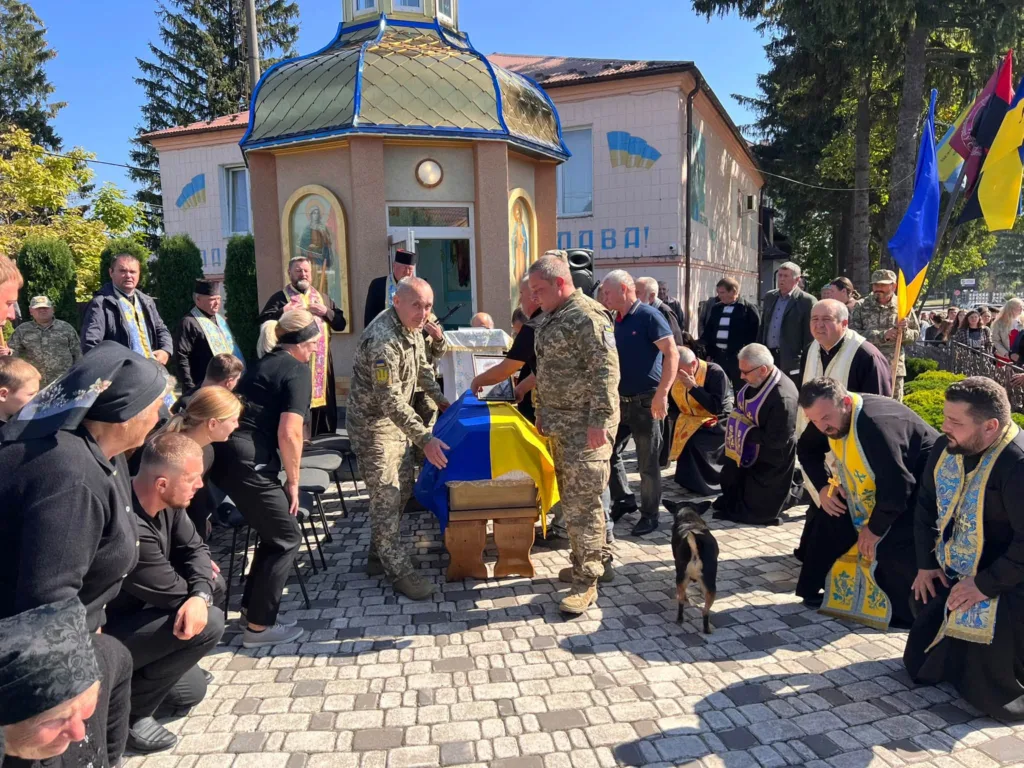 Військові несуть труну, вкриту українським прапором, біля церкви
