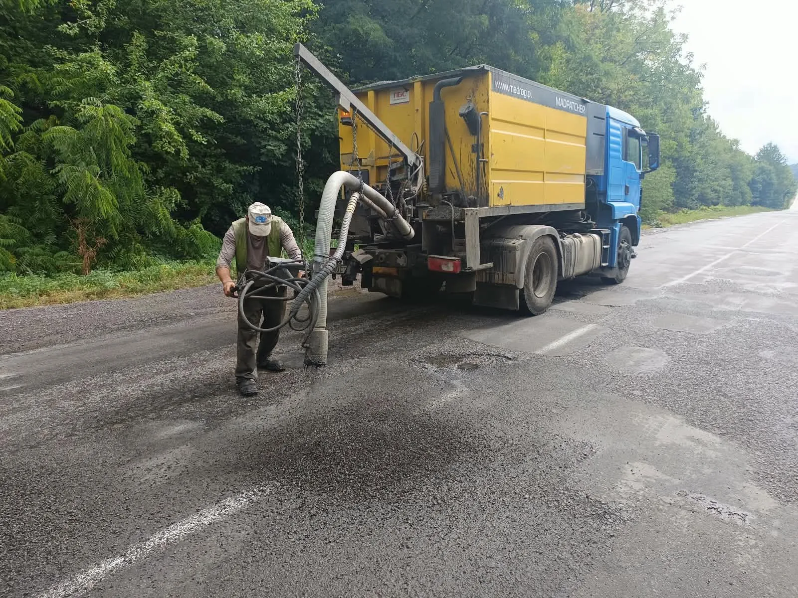Робітник ремонтує асфальт біля дорожньої машини