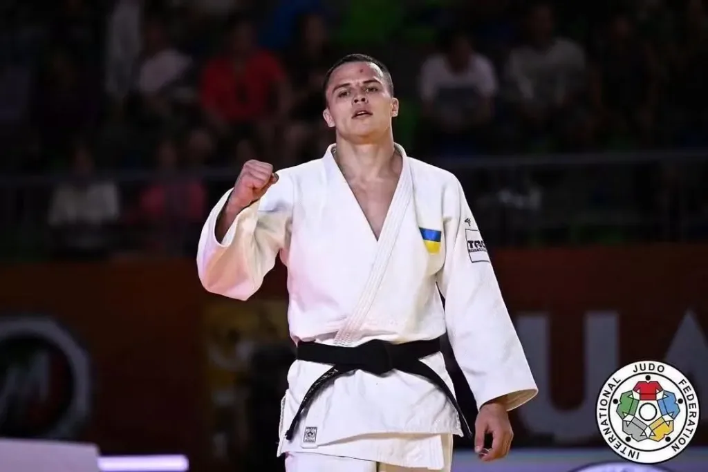 Український дзюдоїст у білому кімоно піднімає кулак