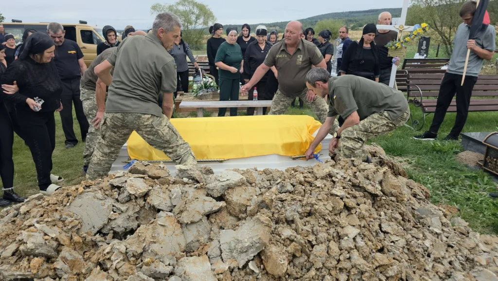 Військові опускають труну, вкриту жовтою тканиною, в могилу