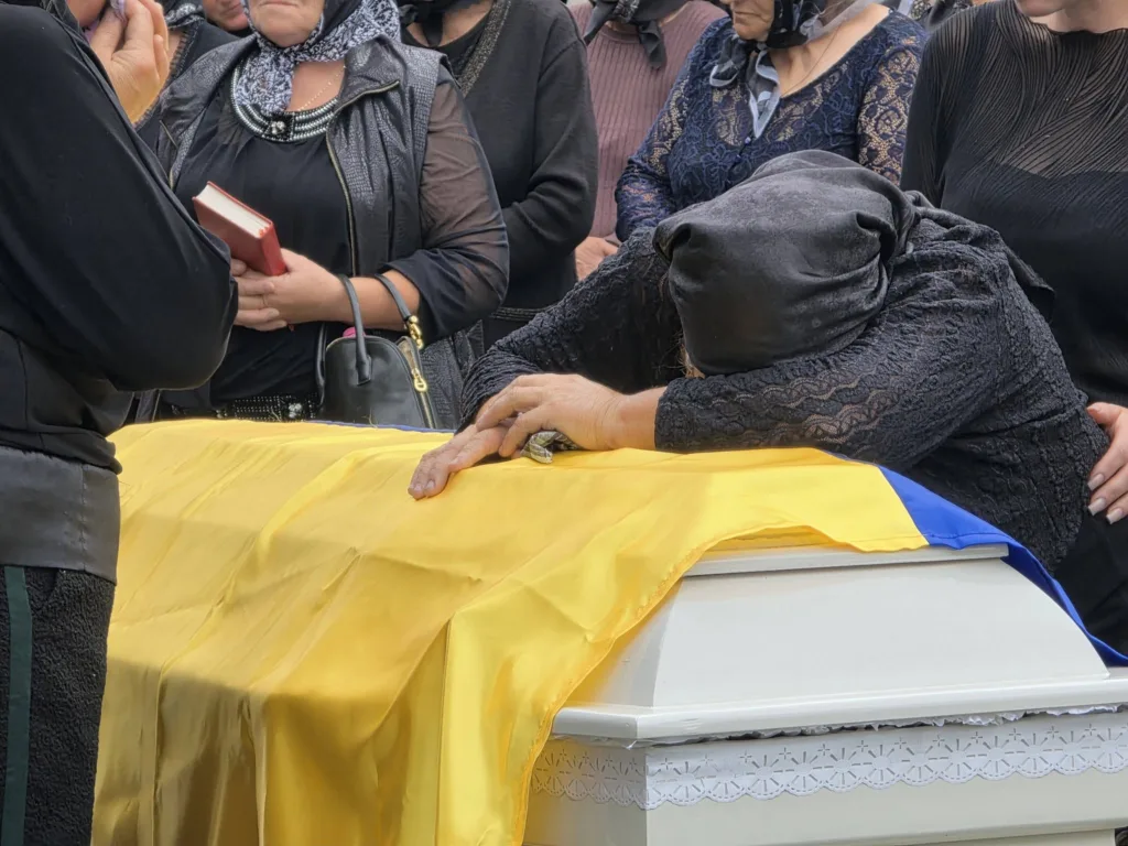 Жінка схилилася над труною, вкритою українським прапором