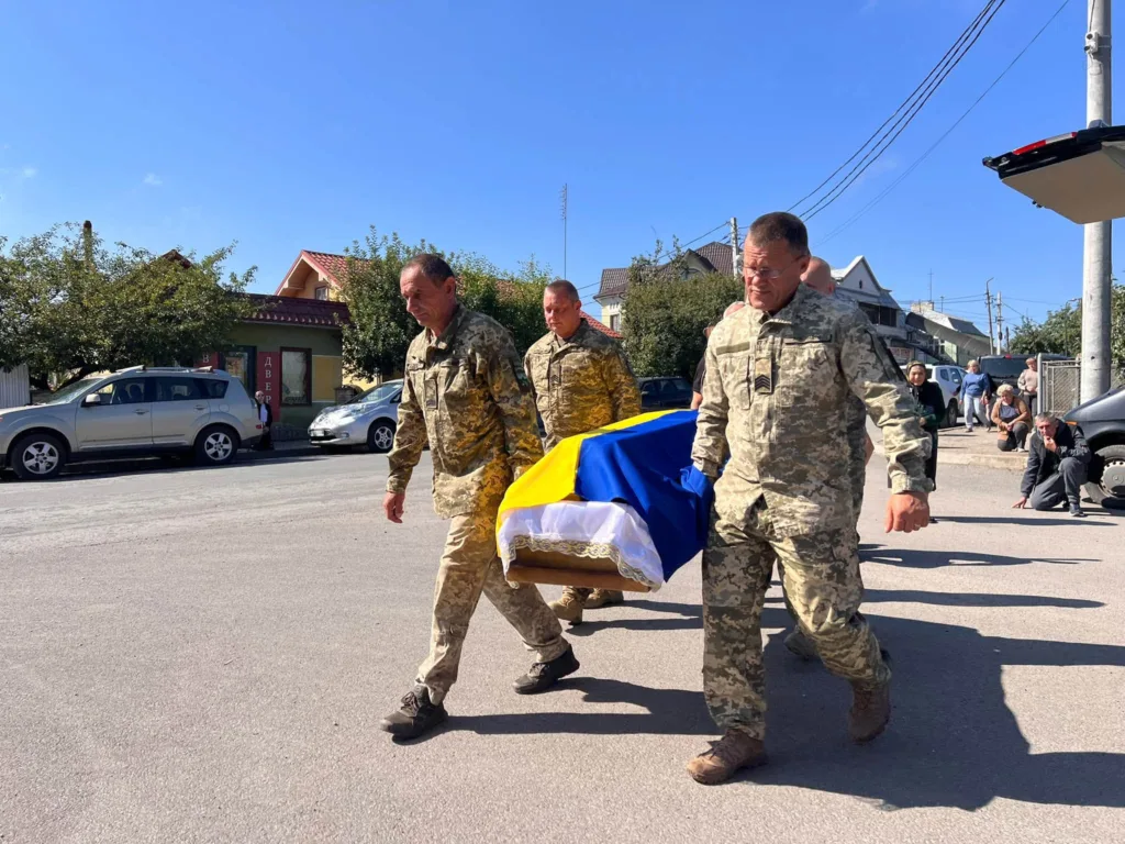 Військові несуть труну, вкриту українським прапором