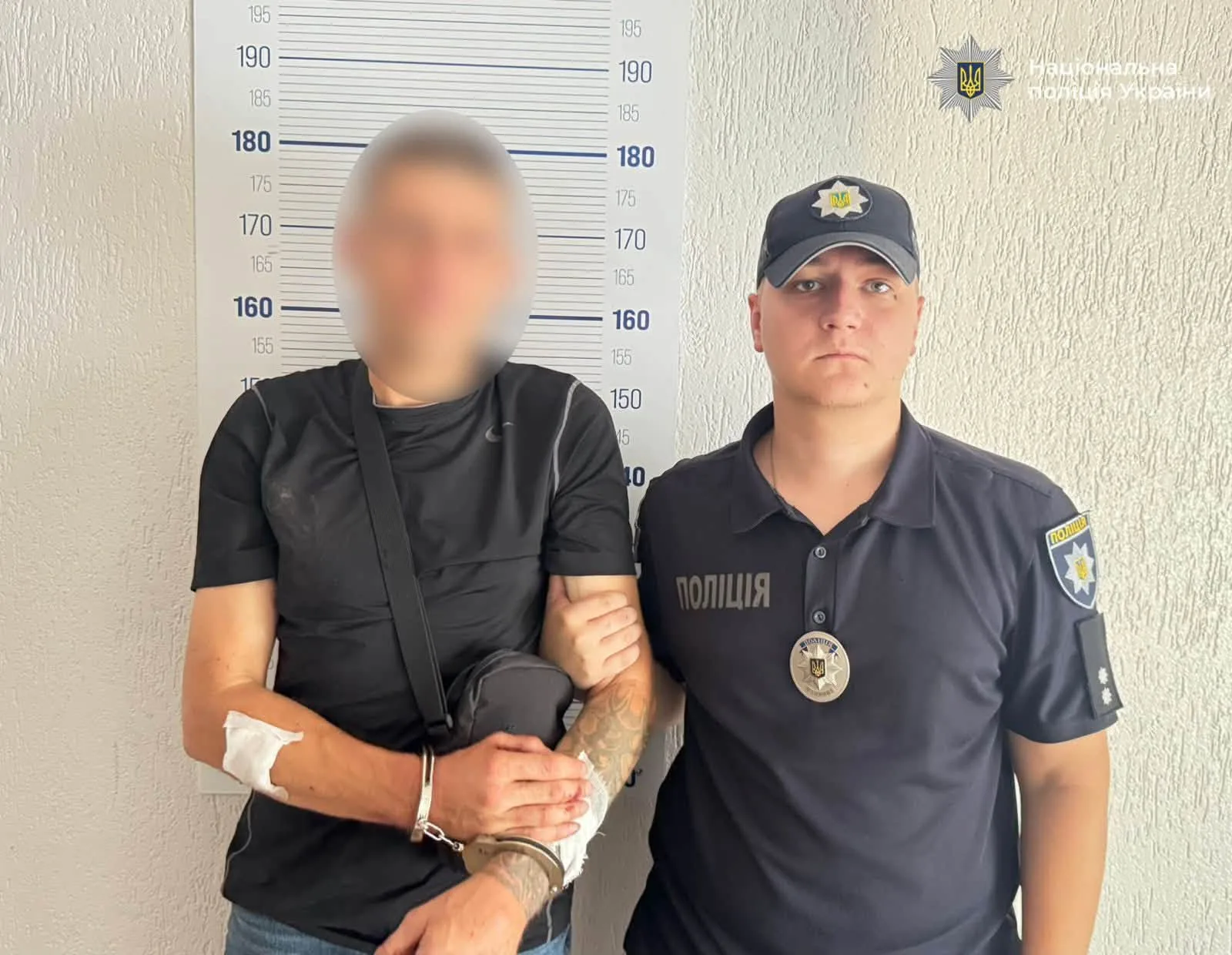 Поліцейський тримає затриманого в кайданках біля ростоміра