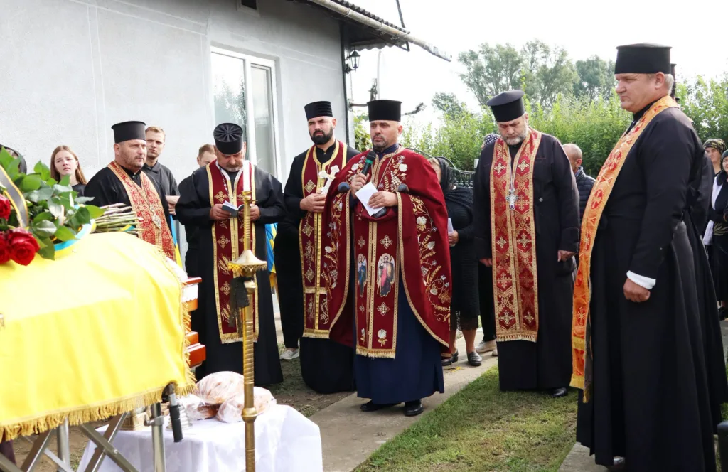Священники проводять заупокійну службу біля труни з прапором