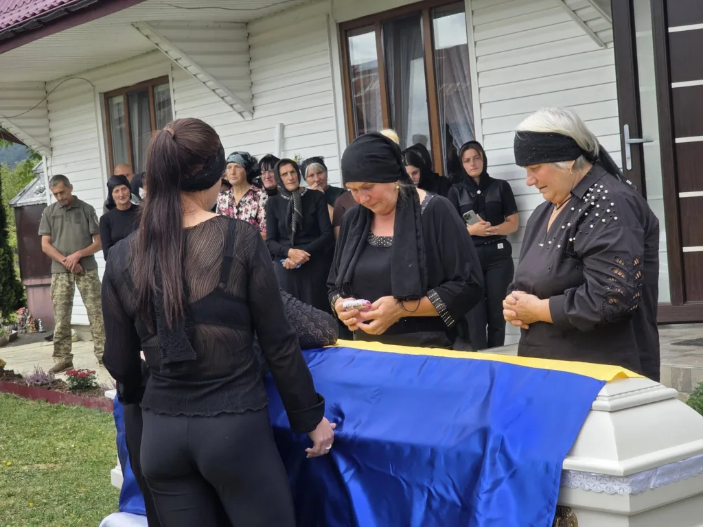 Рідні прощаються з військовим біля труни під прапором України