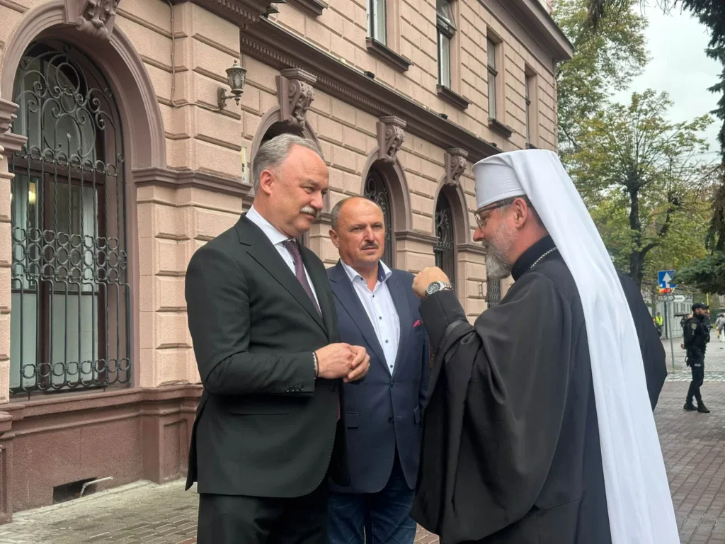 Священнослужитель розмовляє з двома чоловіками біля історичної будівлі