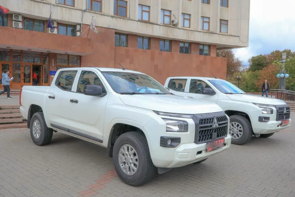 Два білі пікапи Mitsubishi біля адміністративної будівлі