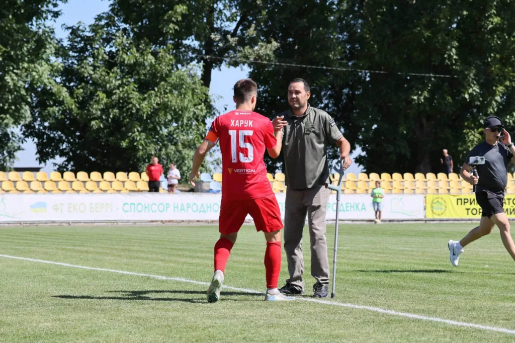 Футболіст у червоній формі вітається з тренером на полі